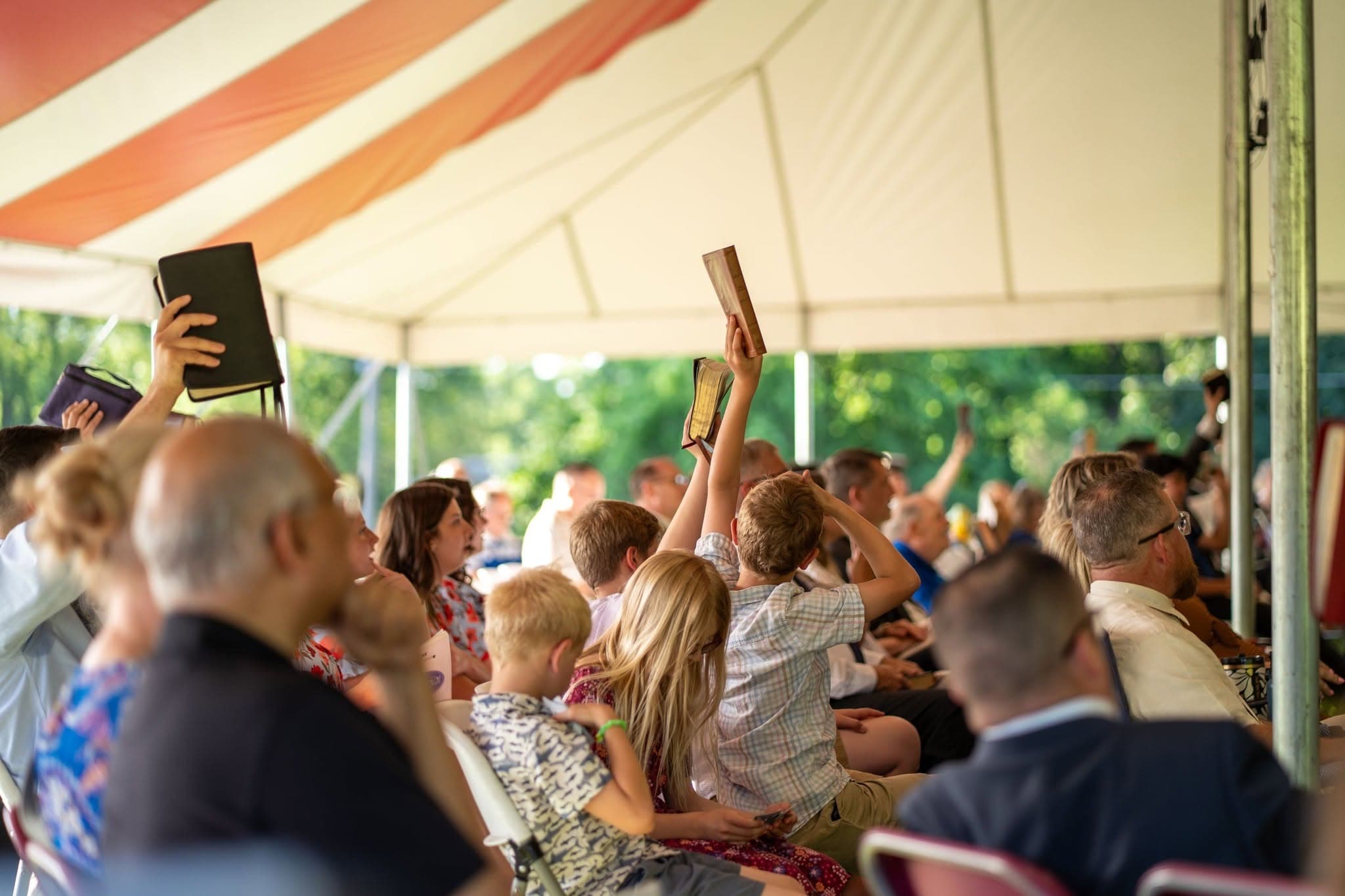 Young people lifting their Bibles during a tent meeting